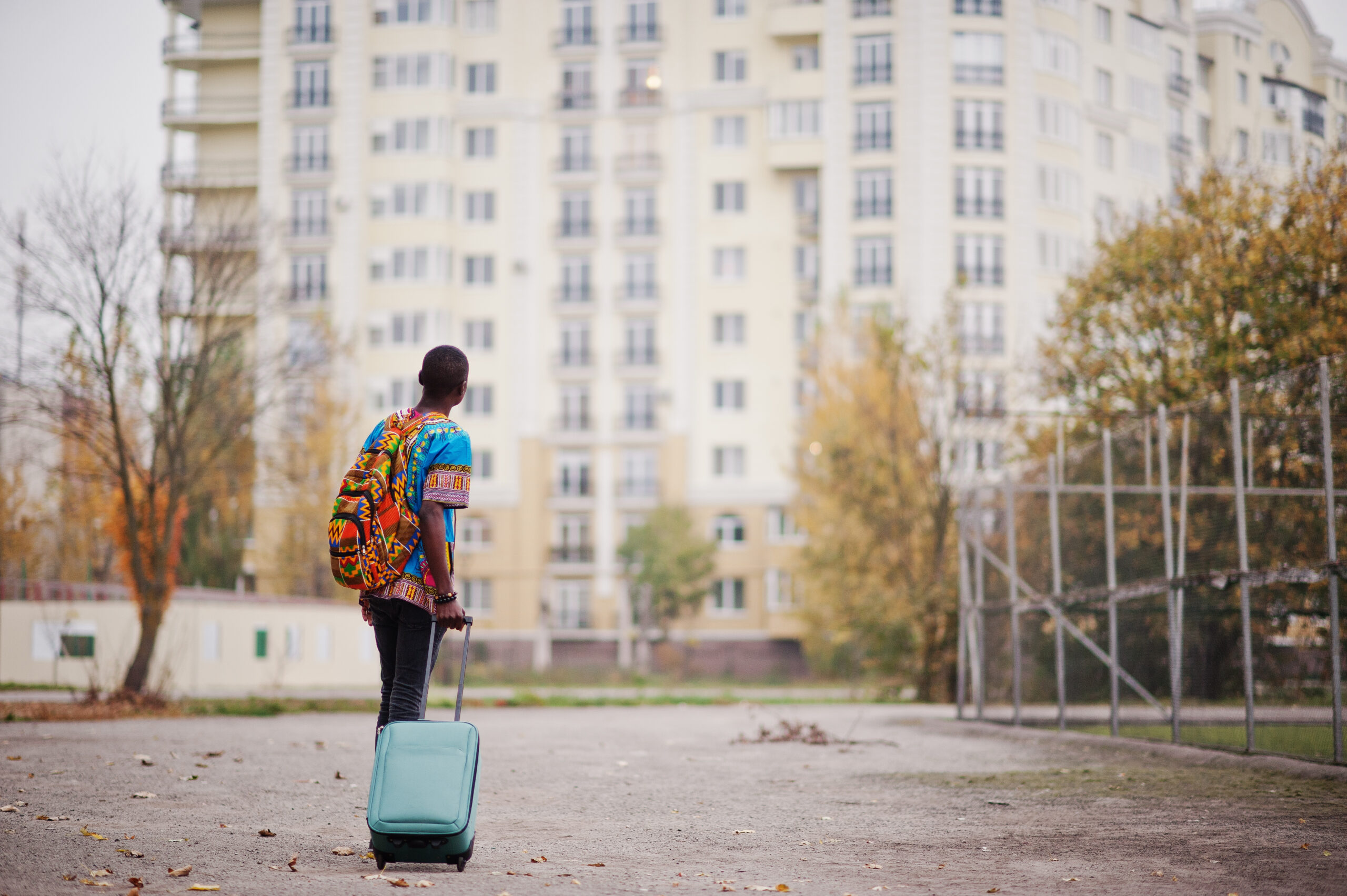A newly arrived migrant with luggage looking at apartment buildings in the UK, symbolising the search for housing as a Global Talent visa holder.