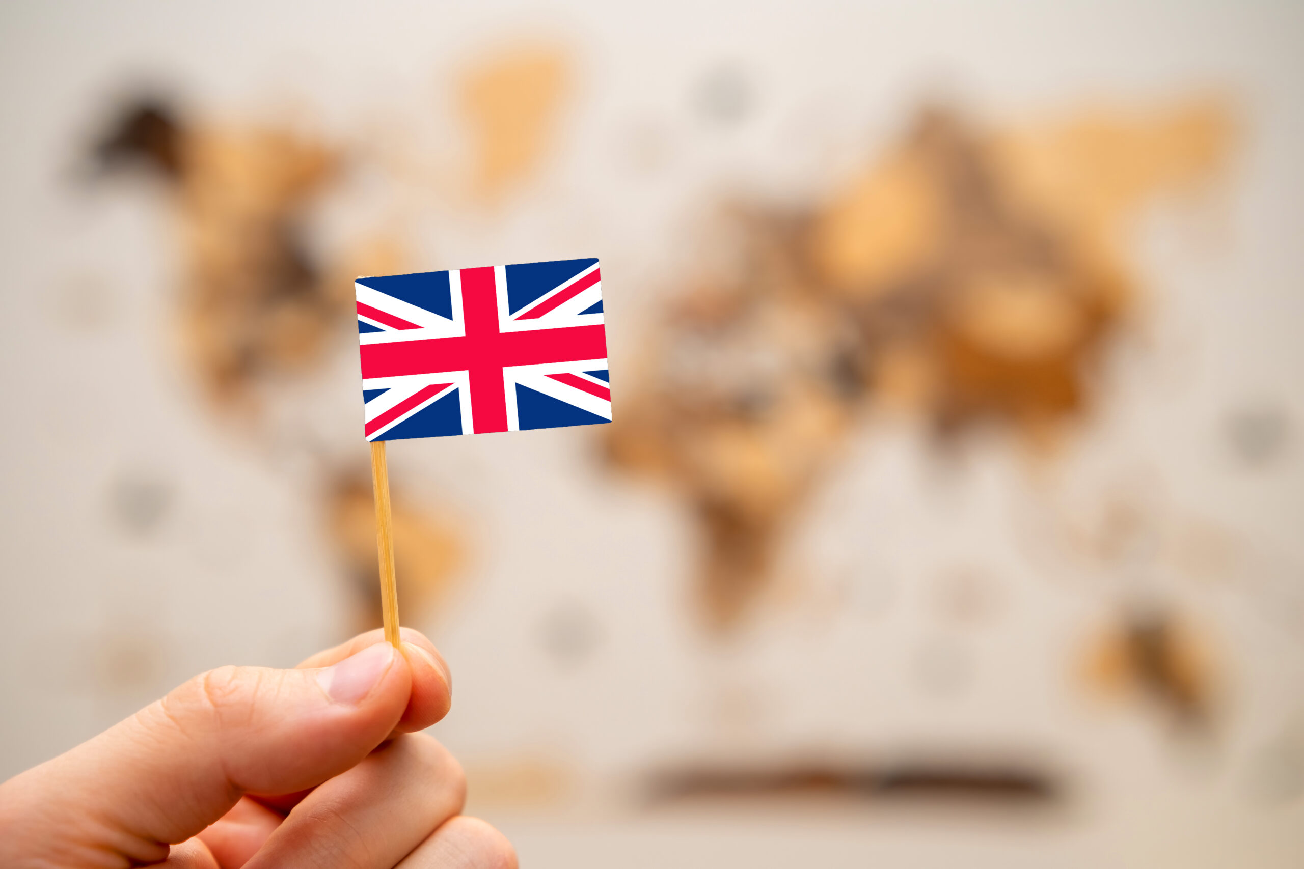 Hand holding a small British flag against a blurred world map background, symbolising UK visas and global mobility.
