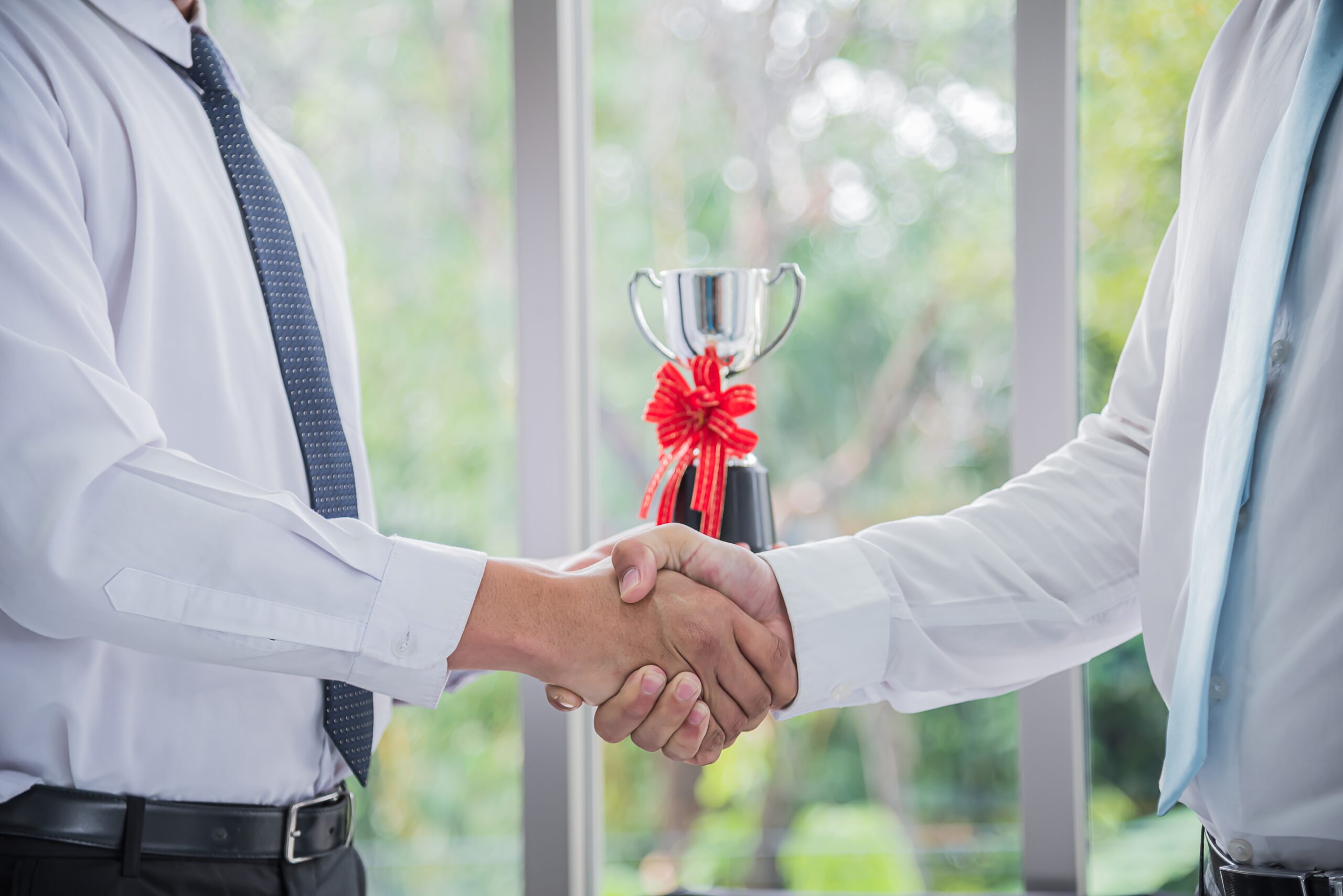 Two professionals shaking hands in front of a trophy, symbolising achievement and recognition, reflecting the difference between recognised talent and exceptional promise under the UK Global Talent visa.