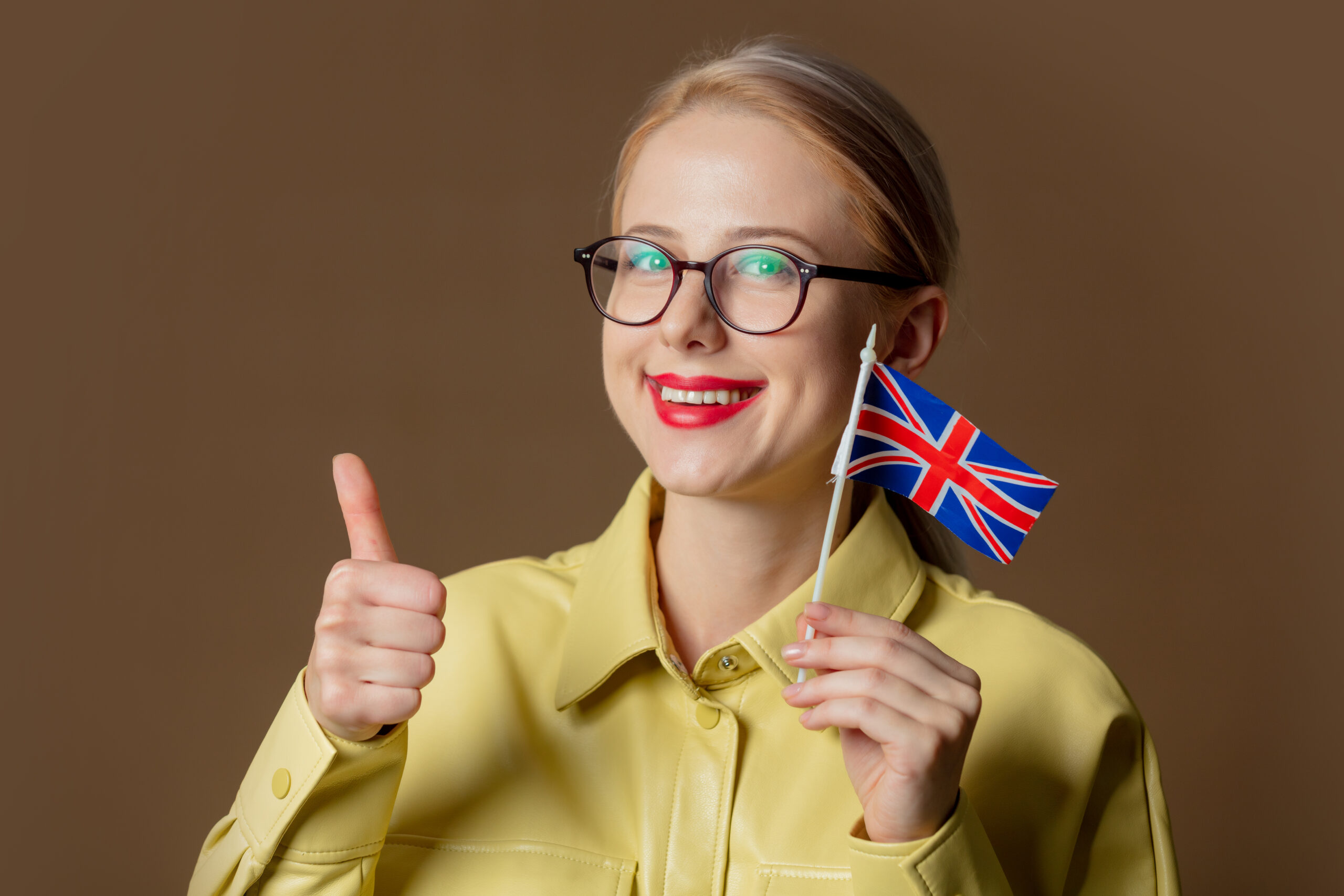 Smiling professional woman holding a UK flag and giving a thumbs up, symbolising success with the Global Talent Visa pathway to ILR.
